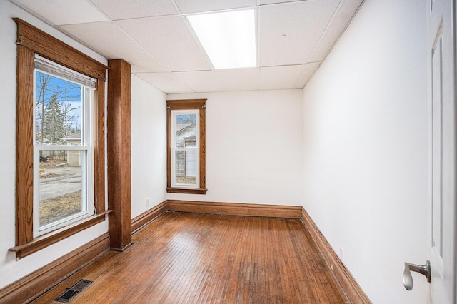 unfurnished room featuring wood-type flooring, visible vents, baseboards, and a drop ceiling