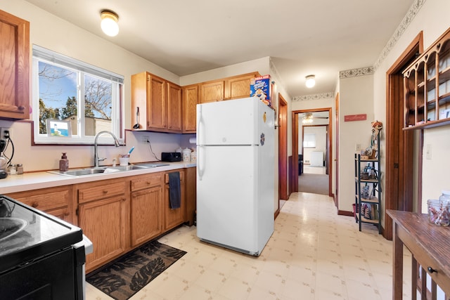 kitchen with black range with electric cooktop, a sink, light countertops, freestanding refrigerator, and light floors