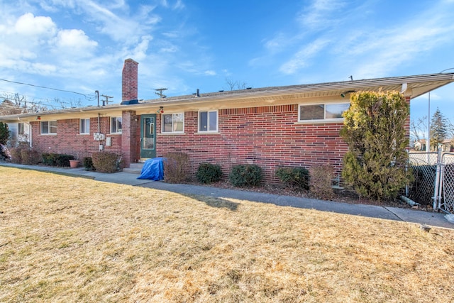 rear view of property with brick siding, a lawn, a chimney, and fence