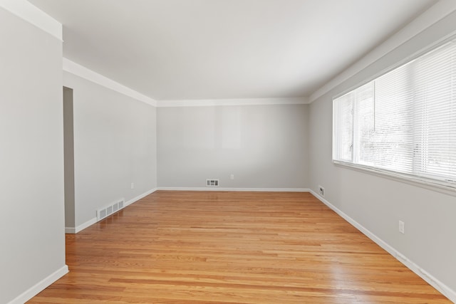 unfurnished room with light wood-type flooring, baseboards, visible vents, and ornamental molding