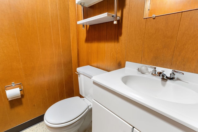 bathroom with toilet, wooden walls, and vanity