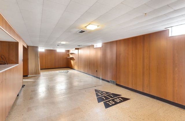 below grade area with light floors, visible vents, wooden walls, and baseboards