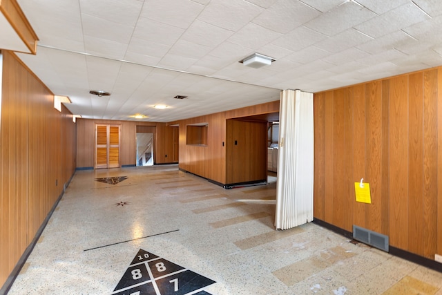 unfurnished room featuring baseboards, wooden walls, visible vents, and speckled floor