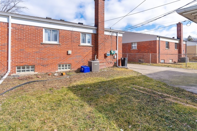 back of property featuring a lawn, a chimney, fence, cooling unit, and brick siding