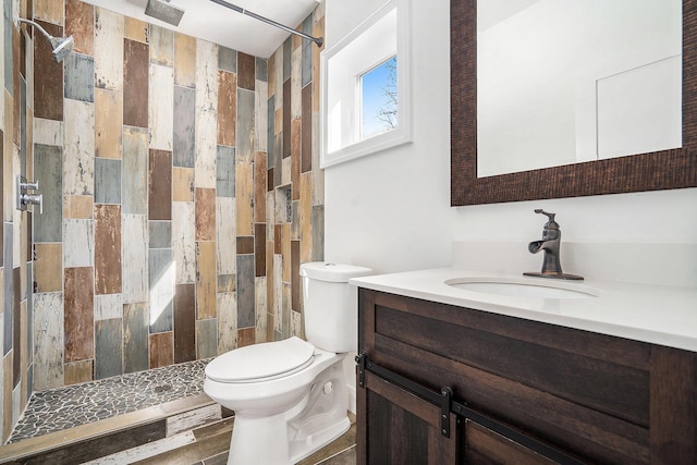 bathroom with toilet, a tile shower, and vanity