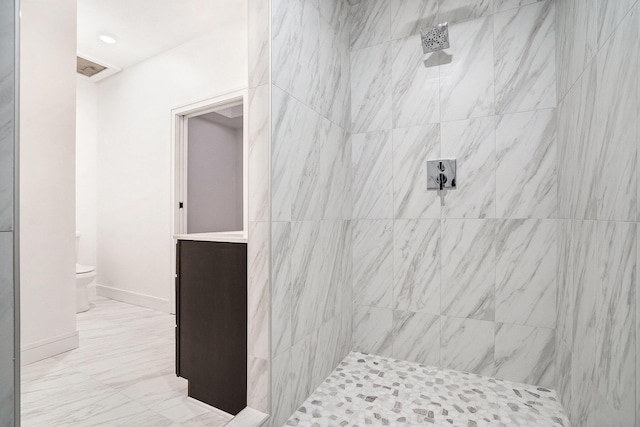 bathroom with tiled shower, toilet, and baseboards