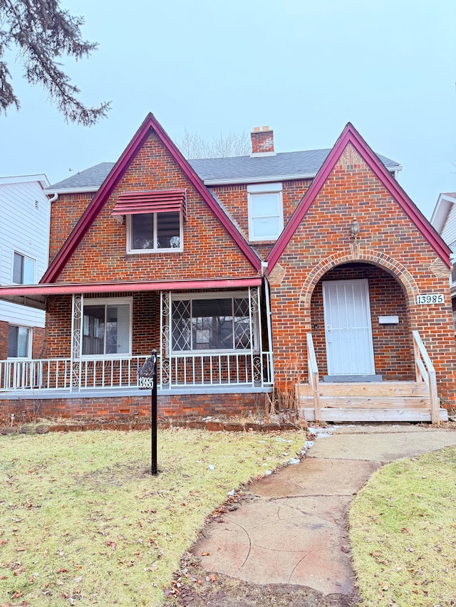 view of front of property featuring a porch, brick siding, a chimney, and a front lawn