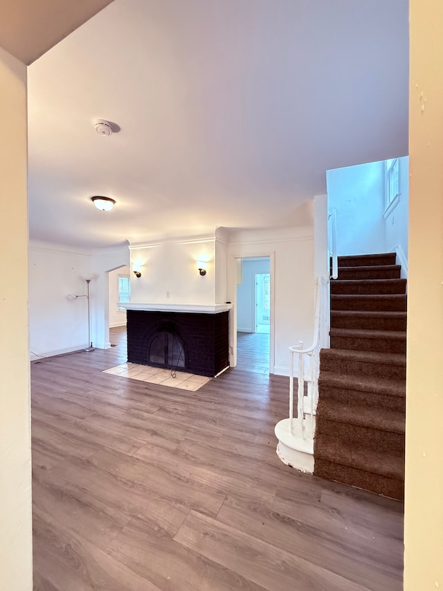 unfurnished living room with stairs, crown molding, a fireplace with flush hearth, and wood finished floors