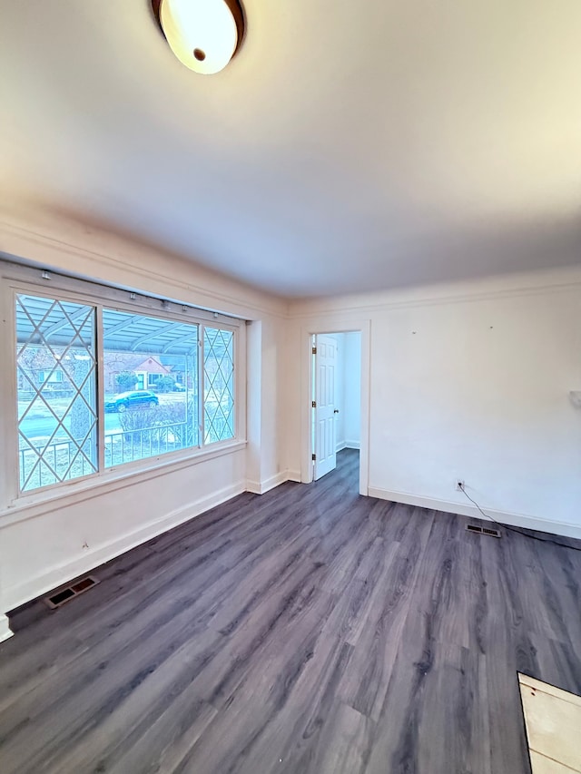 empty room featuring dark wood finished floors, visible vents, and baseboards