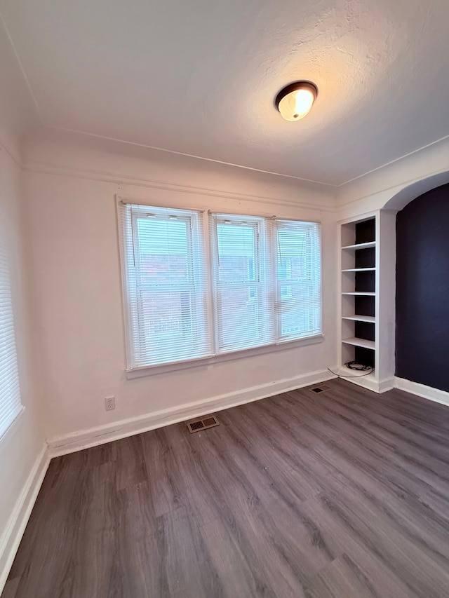 spare room with arched walkways, dark wood finished floors, visible vents, and baseboards