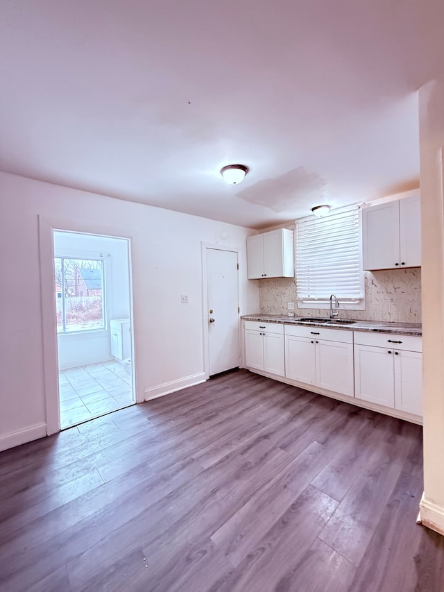 kitchen featuring a sink, wood finished floors, white cabinetry, baseboards, and tasteful backsplash