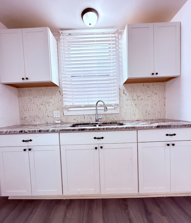 kitchen with light stone counters, a sink, white cabinetry, and decorative backsplash