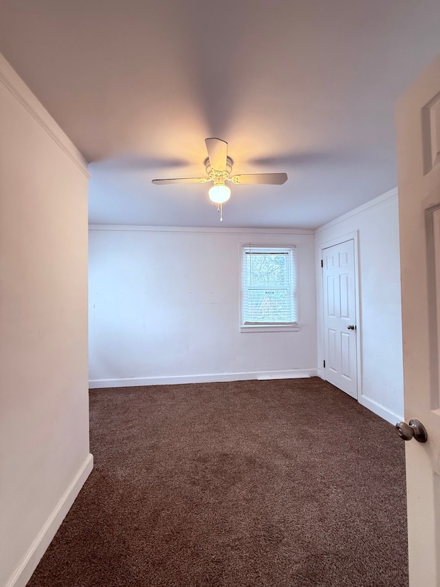 unfurnished room featuring baseboards, dark colored carpet, ceiling fan, and crown molding