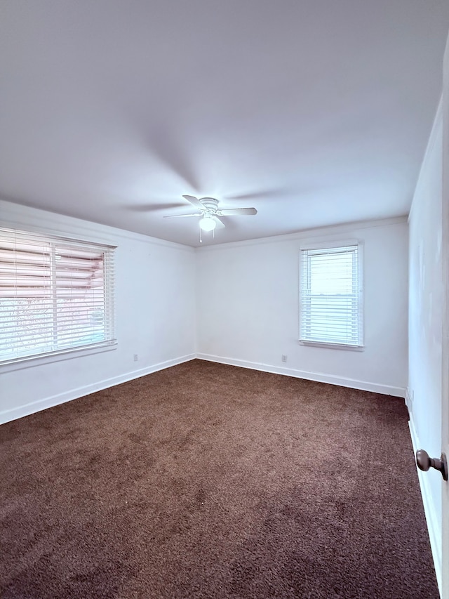 unfurnished room with baseboards, dark carpet, ceiling fan, and crown molding