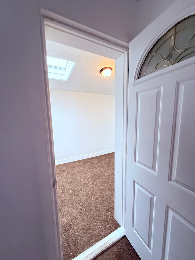 corridor featuring dark carpet, a skylight, and baseboards