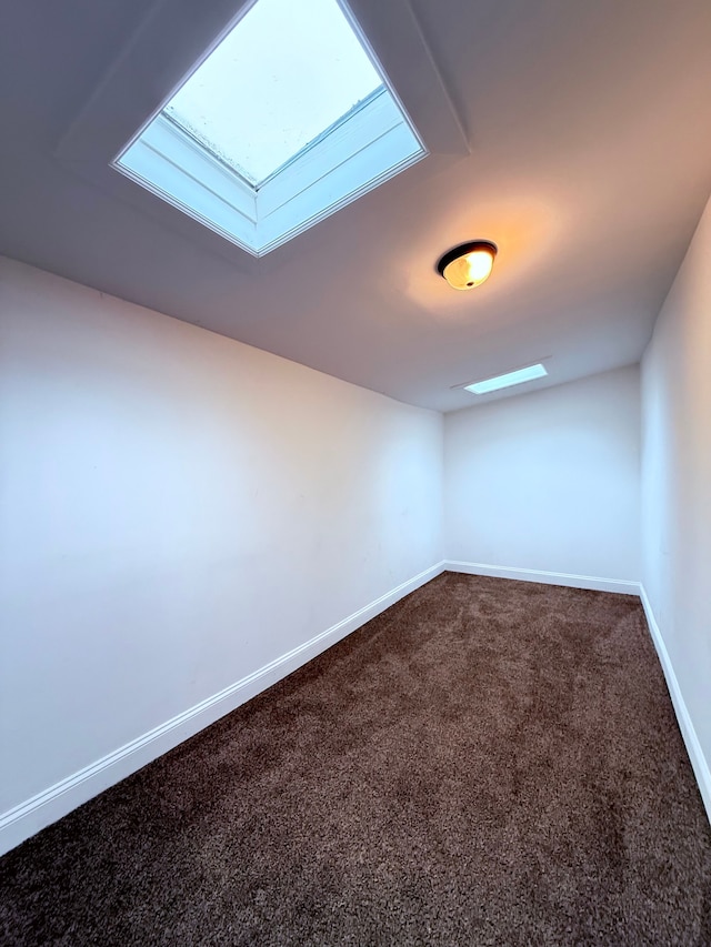 empty room with a skylight, dark carpet, and baseboards