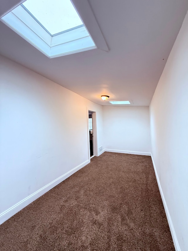 empty room with dark colored carpet, visible vents, baseboards, and a skylight