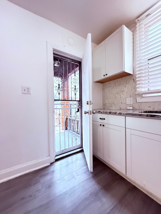 kitchen with tasteful backsplash, baseboards, wood finished floors, stone counters, and white cabinetry