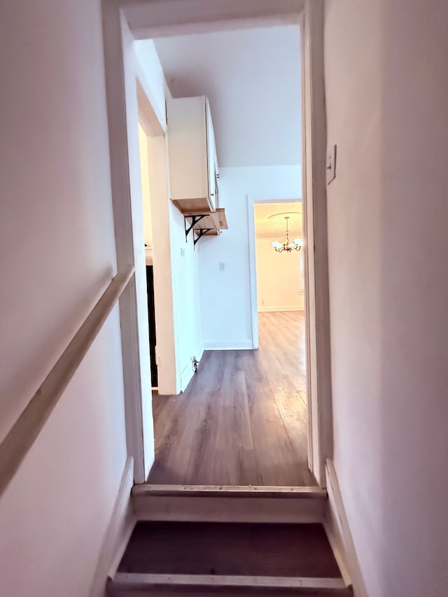 staircase featuring baseboards, an inviting chandelier, and wood finished floors