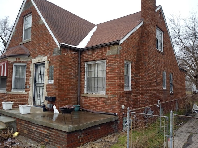 exterior space featuring brick siding, roof with shingles, a chimney, a gate, and fence