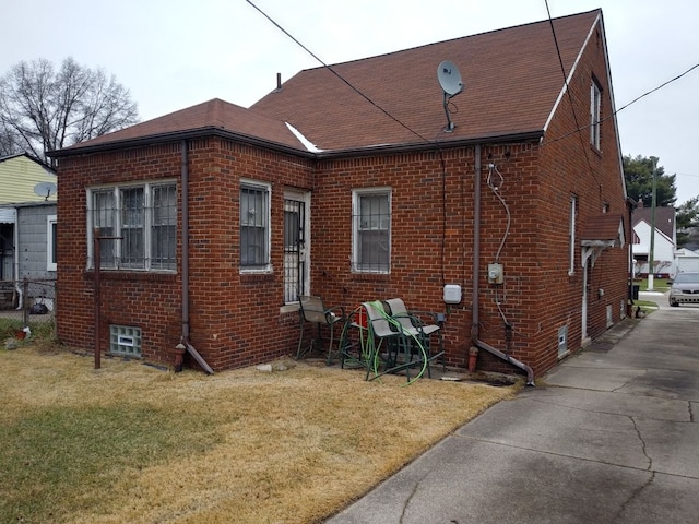 exterior space featuring a shingled roof, brick siding, and a lawn