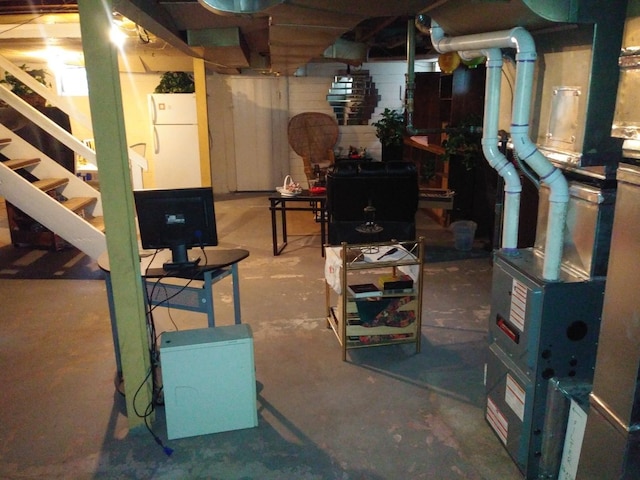 unfinished below grade area featuring freestanding refrigerator, heating unit, and stairs