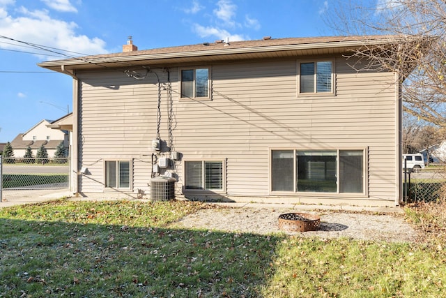 back of house featuring an outdoor fire pit, central air condition unit, fence, a lawn, and a chimney