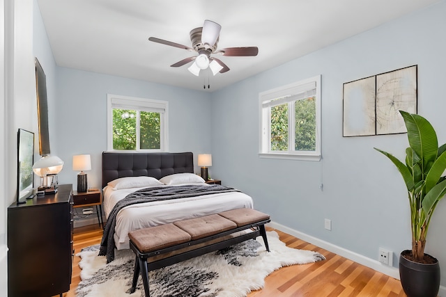 bedroom with ceiling fan, multiple windows, baseboards, and wood finished floors