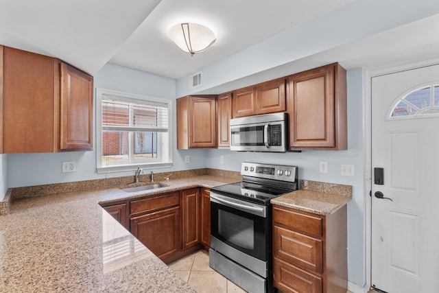 kitchen with brown cabinets, visible vents, appliances with stainless steel finishes, light tile patterned flooring, and a sink