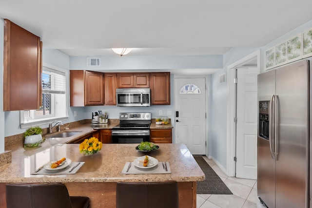 kitchen featuring brown cabinets, stainless steel appliances, visible vents, a sink, and a peninsula