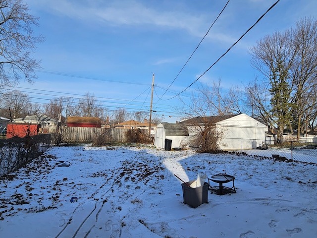 yard covered in snow featuring a storage shed, a fenced backyard, a fire pit, and an outbuilding