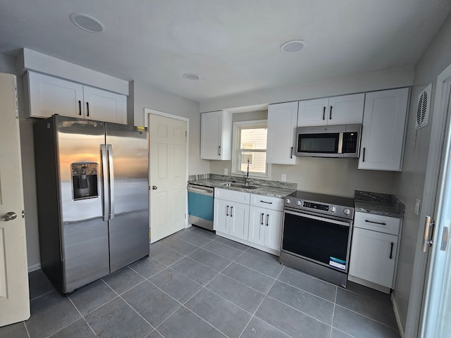 kitchen with appliances with stainless steel finishes, white cabinetry, a sink, dark stone countertops, and dark tile patterned floors