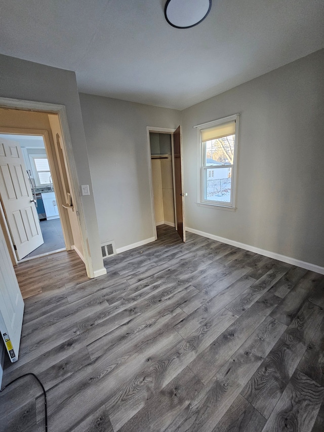 unfurnished bedroom with dark wood-style floors, a closet, visible vents, and baseboards