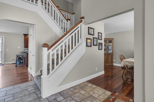 stairs with a towering ceiling, baseboards, and wood finished floors