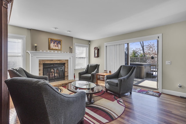 living area with wood-type flooring, a wealth of natural light, and a brick fireplace