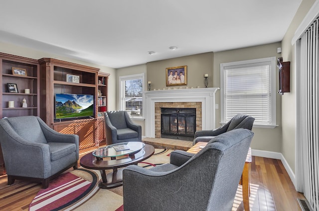 living area featuring a brick fireplace, visible vents, baseboards, and wood finished floors