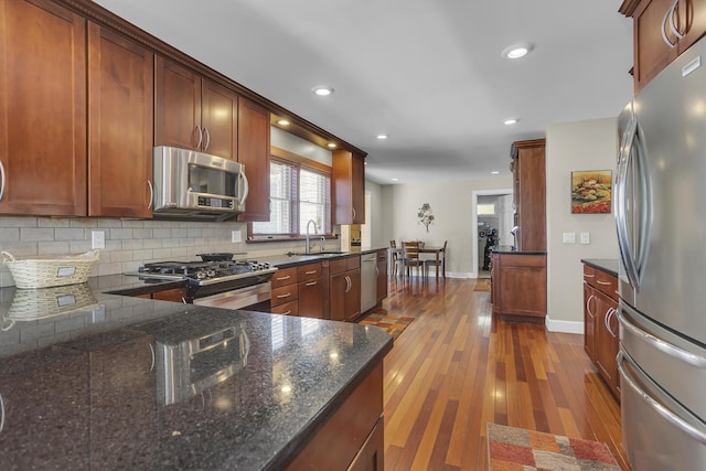 kitchen with decorative backsplash, dark wood-style flooring, dark stone countertops, stainless steel appliances, and a sink