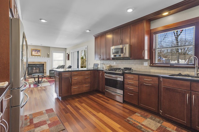 kitchen with stainless steel appliances, dark countertops, backsplash, open floor plan, and a sink