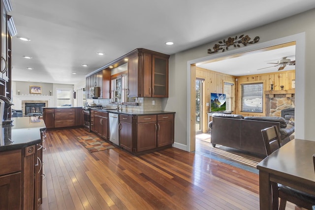 kitchen with open floor plan, a stone fireplace, dark wood-style floors, and stainless steel dishwasher