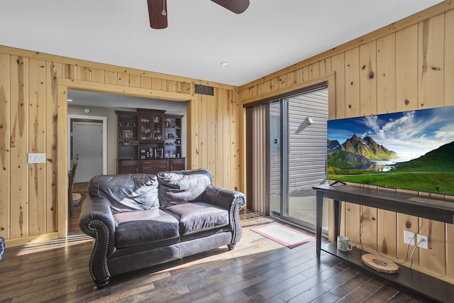 living area with dark wood-style flooring, wood walls, and a ceiling fan