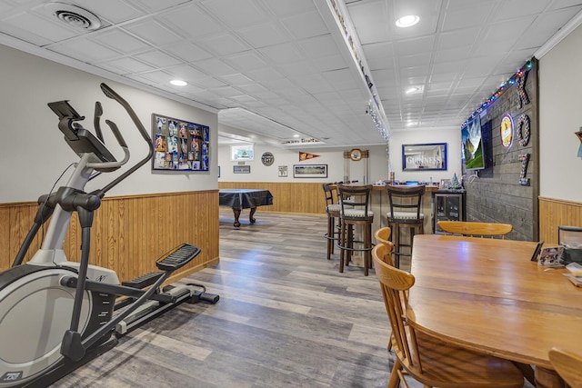 exercise room with beverage cooler, wooden walls, a wainscoted wall, wood finished floors, and a bar