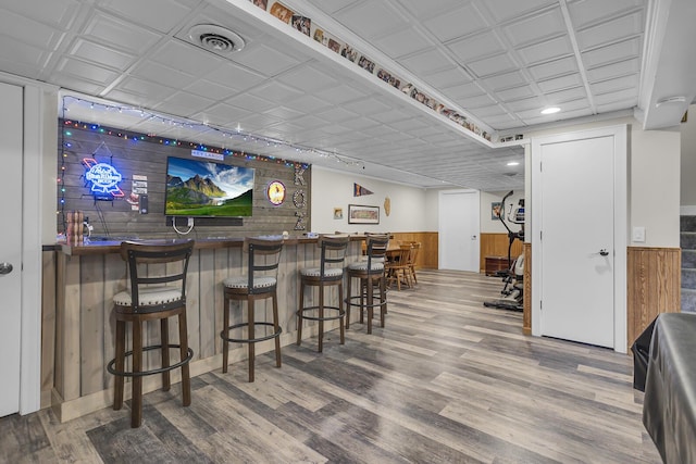 bar with a dry bar, wooden walls, visible vents, a wainscoted wall, and wood finished floors