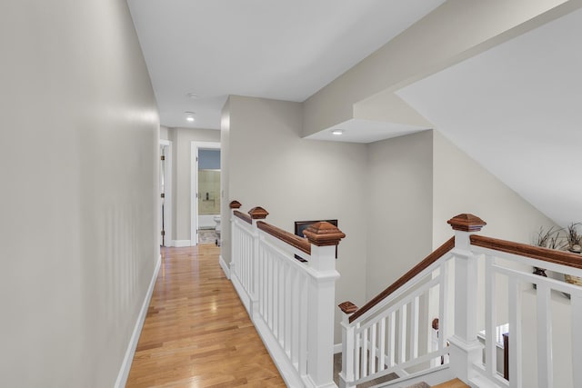 hallway featuring light wood-style flooring, baseboards, and an upstairs landing