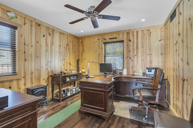 home office with a wood stove, wood walls, a ceiling fan, and dark wood-style flooring