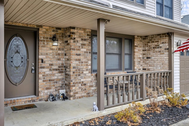 property entrance with a garage, a porch, and brick siding