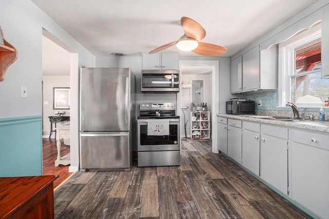 kitchen featuring dark wood finished floors, a ceiling fan, appliances with stainless steel finishes, light countertops, and a sink