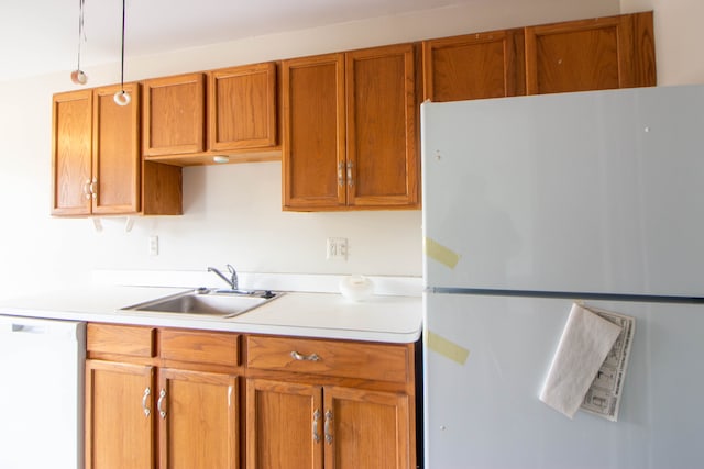 kitchen with light countertops, white appliances, brown cabinetry, and a sink