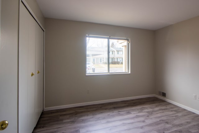 unfurnished bedroom featuring visible vents, a closet, baseboards, and wood finished floors