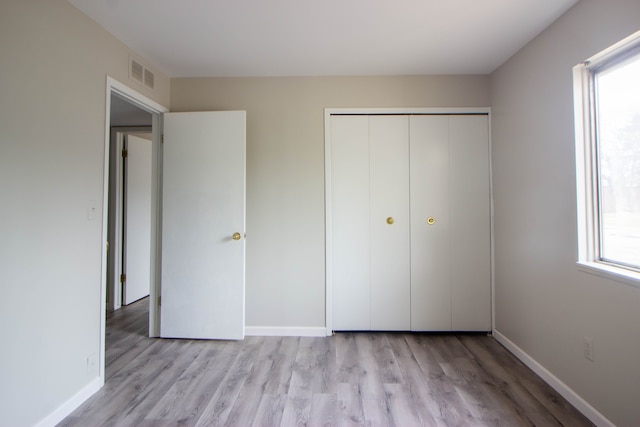 unfurnished bedroom featuring light wood-style floors, baseboards, visible vents, and a closet