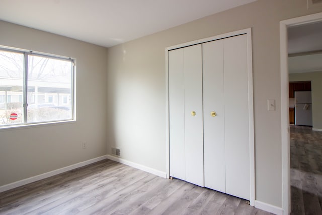 unfurnished bedroom with baseboards, visible vents, freestanding refrigerator, light wood-type flooring, and a closet